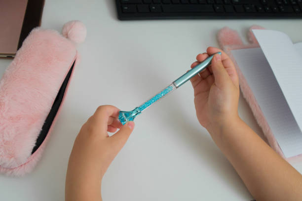 istock A child is holding a blue ball pen in its hands and looking at it. The pencil case, notebook, monitor, and smartphone are aside on the table. First-person view 1333925131