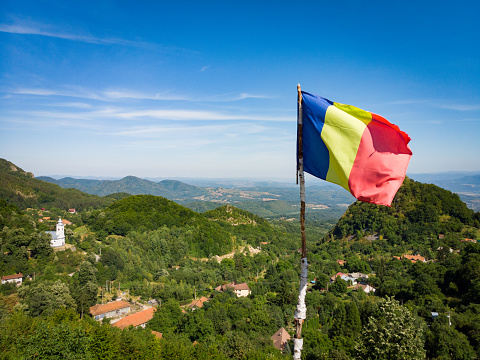 The Romanian flag flies proudly over a lush green landscape in the Transylvania region of Romania.