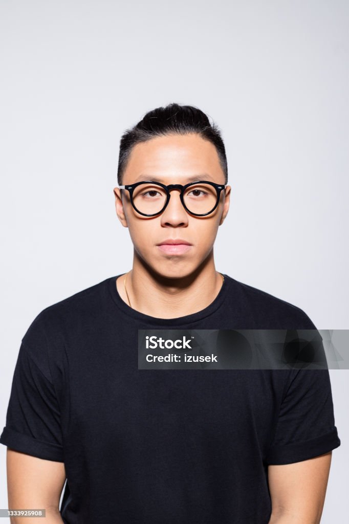 Worried asian young man in black clothes Portrait of handsome asian young man wearing black t-shirt and eyeglasses, looking at camera. Studio shot, grey background. Men Stock Photo