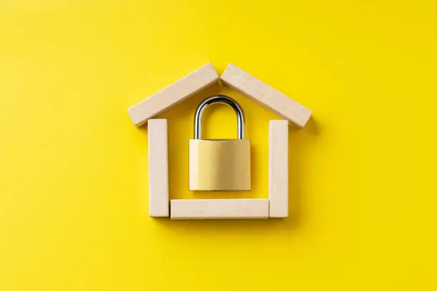 Photo of house symbol made by wooden blocks over yellow background with padlock inside. outer space. home protection and security concept
