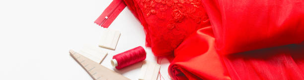 istock Sewing accessories concept. Hobby sewing with thread, scissors, red satin fabric. White background top view. 1333927290