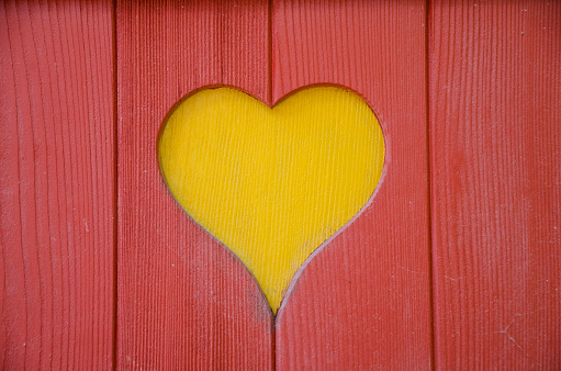 A heart shape was cut out of wood. The red wooden planks have been placed on a yellow background. The photo was taken in Switzerland. There is copy space for your own text.