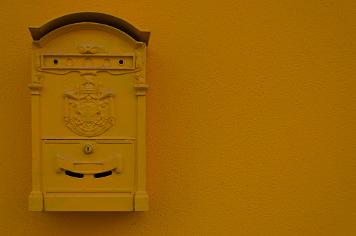 The background image shows an old postbox, which is hanging at a yellow painted wall. There is copy space to the right of the letterbox.