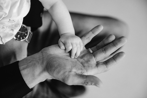 Hand of small child on palm of dad in close-up. Father holds hand of newborn in his hand. Family: parent and baby hands. Concept of parenting, parental care and Father's Day. Copy space for image site