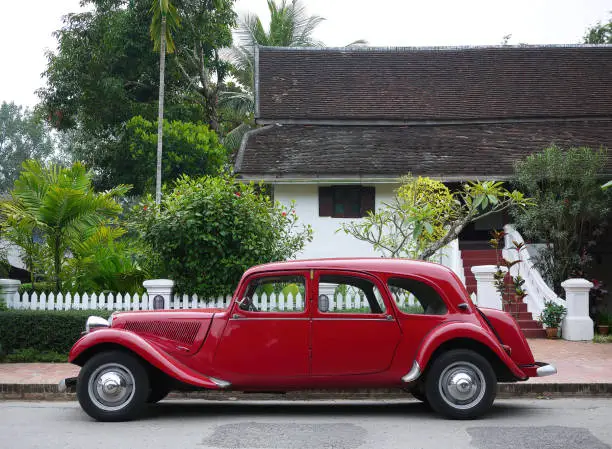 Photo of Classic red Citroen Traction Avant vintage car side view against backdrop of colonial heritage buildings