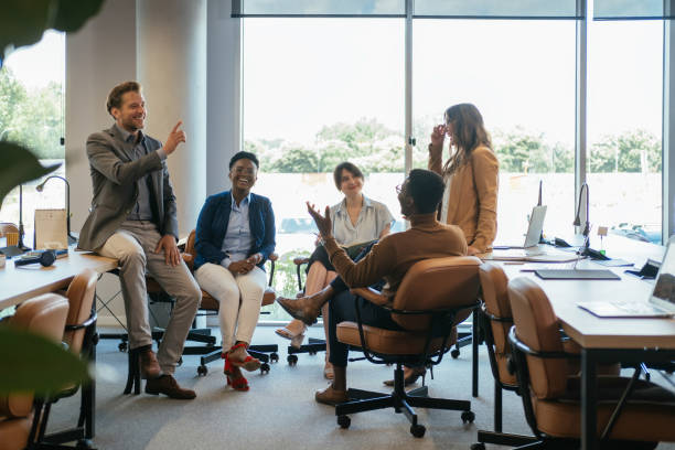 Group of Smiling Businesspeople in a Casual Meeting at their Company Team of five multi-ethnic employee having fun working together in an open plan office with big windows. corporate culture stock pictures, royalty-free photos & images