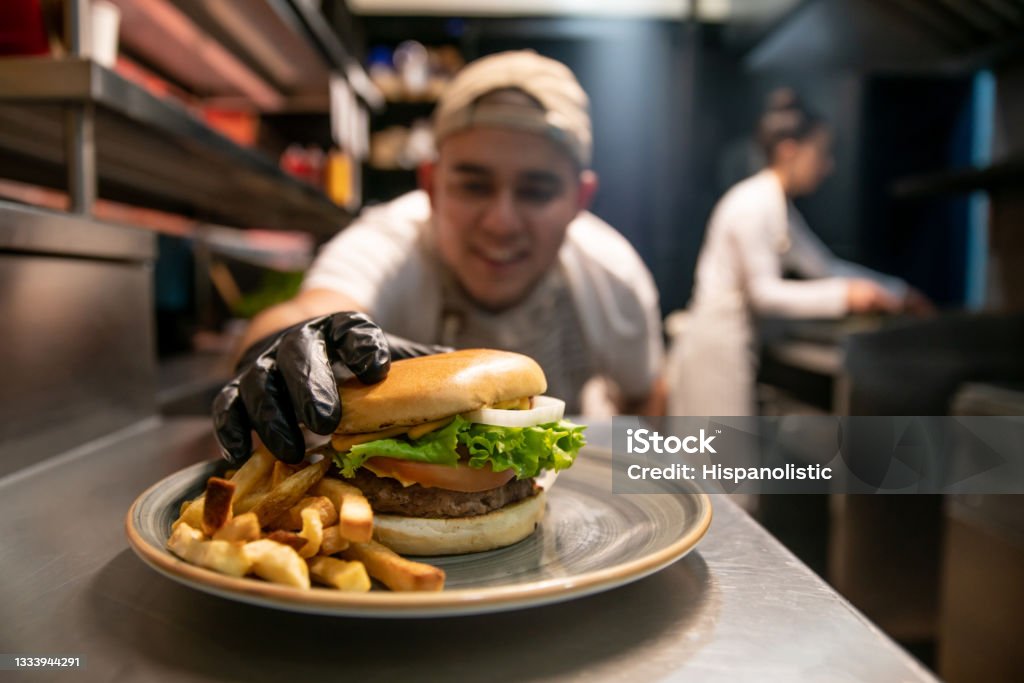 Happy chef preparing burgers at a fast food restaurant Happy Latin American chef preparing burgers at a fast food restaurant - eating out concepts Chef Stock Photo