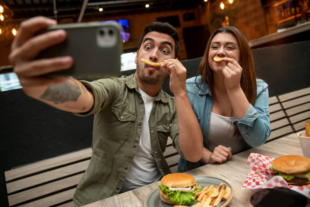 casal tirando uma selfie engraçada enquanto comia em um restaurante - dating couple love latin american and hispanic ethnicity - fotografias e filmes do acervo