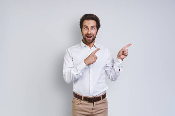 istock Handsome young smiling man in white shirt looking at camera and pointing away 1333946534