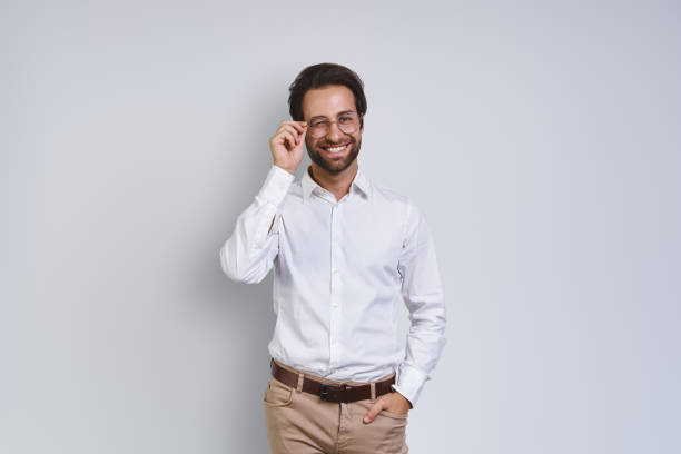 istock Handsome young man in white shirt looking at camera and adjusting his eyeglasses 1333946564