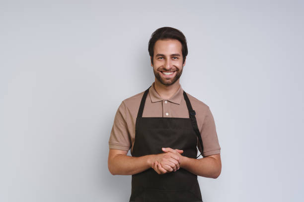 istock Handsome young man in apron looking at camera and keeping hands clasped 1333946715