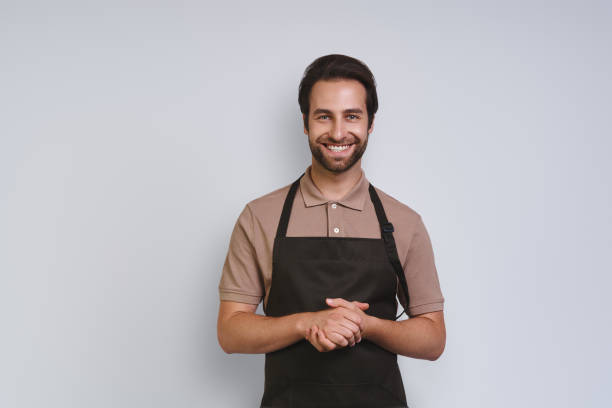Handsome young man in apron looking at camera and keeping hands clasped stock photo