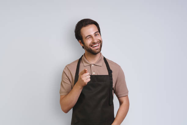 Handsome young man in apron looking at camera and pointing you