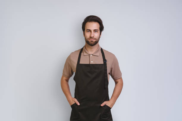istock Handsome young man in apron looking at camera and holding hands on hip 1333946735