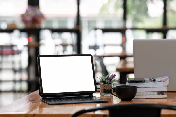 istock Mockup blank screen tablet with magic keyboard on wooden table in cafe room. 1333946786