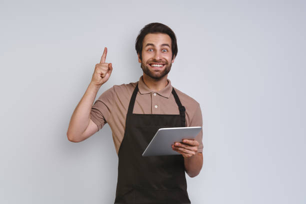 istock Cheerful young man in apron showing his digital tablet and gesturing 1333948468