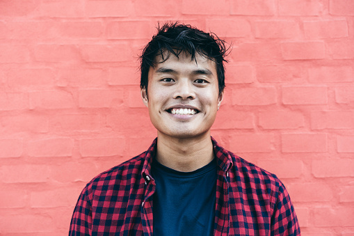 Happy Asian guy portrait - Confident asian young male having fun smiling while posing in front of camera against a red wall background