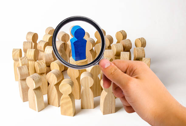 a magnifying glass looks at the blue figure of a man in the center of a crowd of people. leadership and team management, an example for imitation. loyalty and trust. idol followers - surrounding leadership organization meeting imagens e fotografias de stock