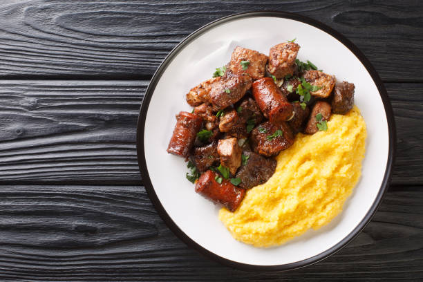 揚げ豚肉、ソーセージ、オフラルのフライドポテトで構成されるルーマニアのお祝いの料理ポマナポルキュイは、プレート上にトウモロコシのおかゆをクローズアップして提供します。水平� - polenta ストックフォトと画像