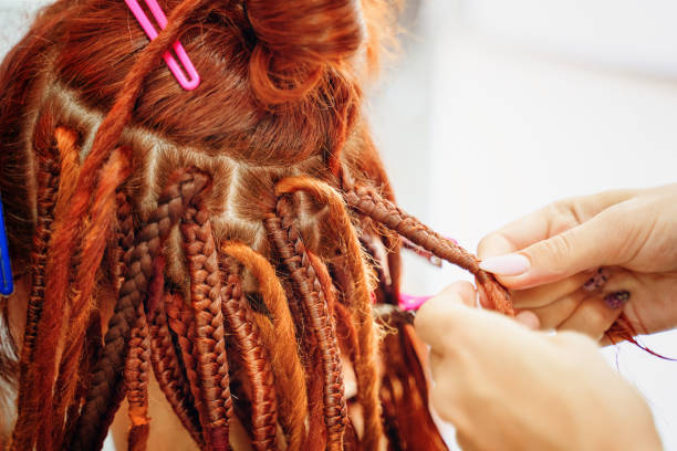 istock Hairdresser's hands braid girl's ginger dreadlocks. 1333954176