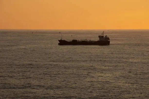 A trade cargo ship sailing alone at the sea in the Atlantic Ocean during sunset. High quality photo