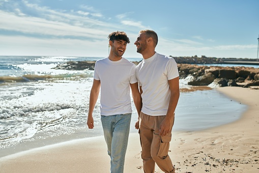 Young gay couple smiling happy walking at the beach.