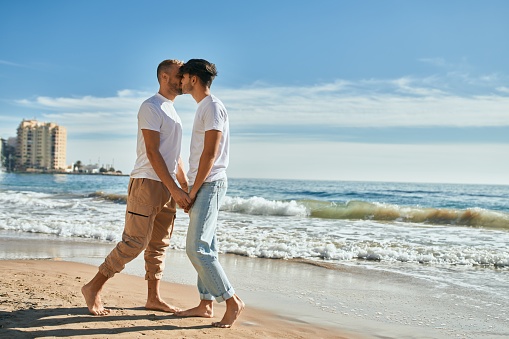 Young gay couple kissing at the beach.