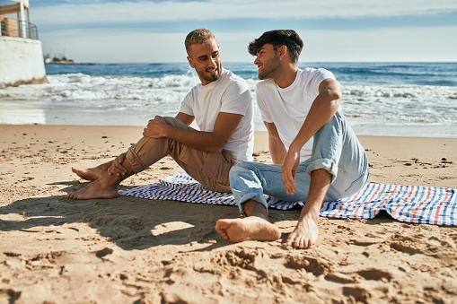 Young gay couple smiling happy sitting at the beach.