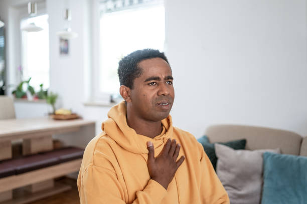 Adult man with pain in chest Adult man wearing yellow hoodie touching his chest in pain. male chest pain stock pictures, royalty-free photos & images