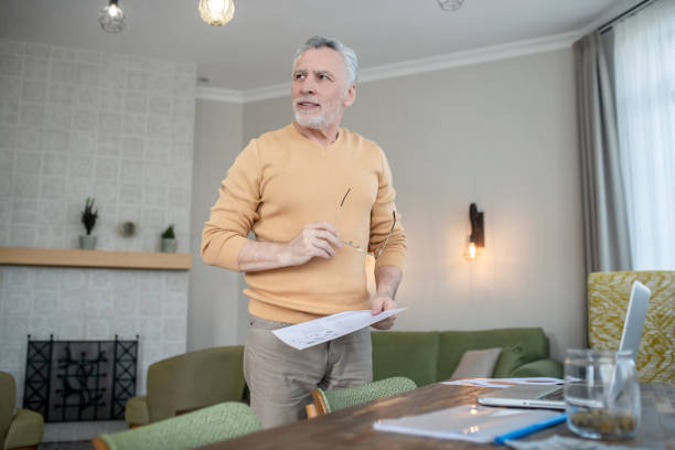 istock Gray-haired man in eyewear looking busy while working with project papers 1333957983
