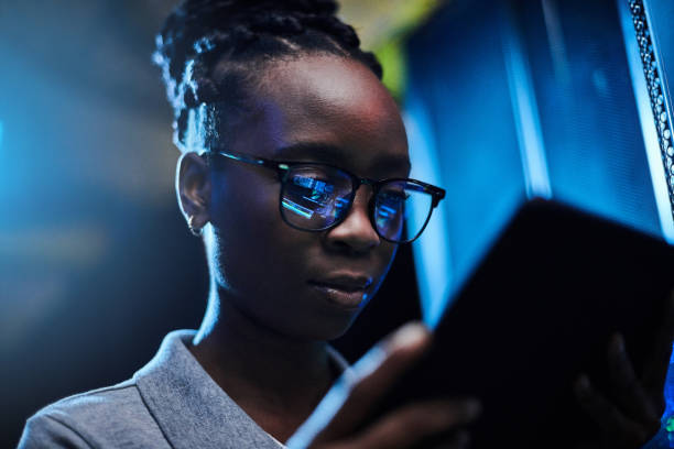 Shot of a young female engineer using a digital tablet while working in a server room She'll keep you connected and your data protected black nerd stock pictures, royalty-free photos & images