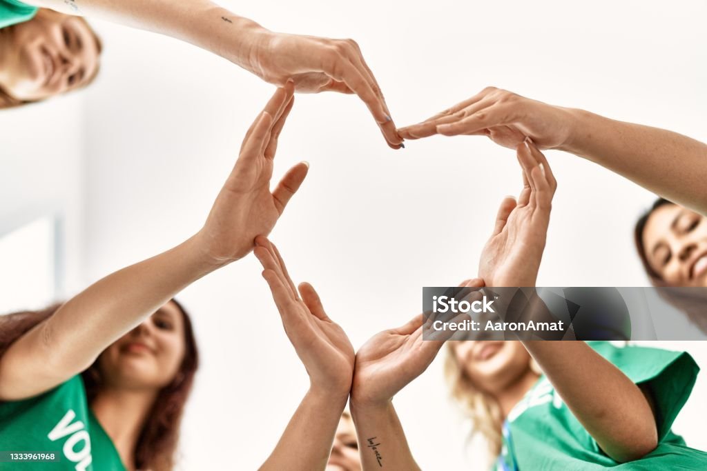 Group of young volunteers woman smiling happy make heart symbol with hands together at charity center. Charity and Relief Work Stock Photo