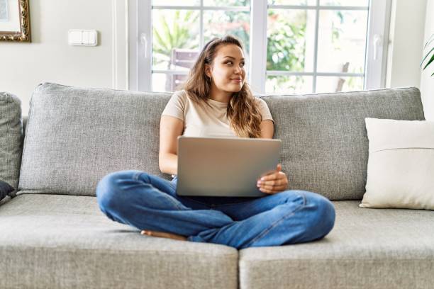 istock Beautiful young brunette woman sitting on the sofa using computer laptop at home smiling looking to the side and staring away thinking. 1333964908