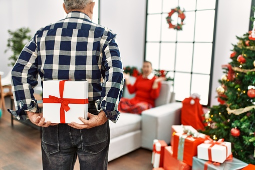 Young daughter and senior father together celebrating christmas at home, parent giving present to woman