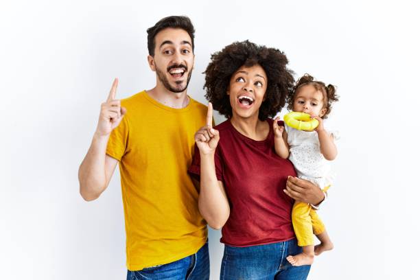 interracial young family of black mother and hispanic father with daughter smiling amazed and surprised and pointing up with fingers and raised arms. - mother holding child pointing imagens e fotografias de stock