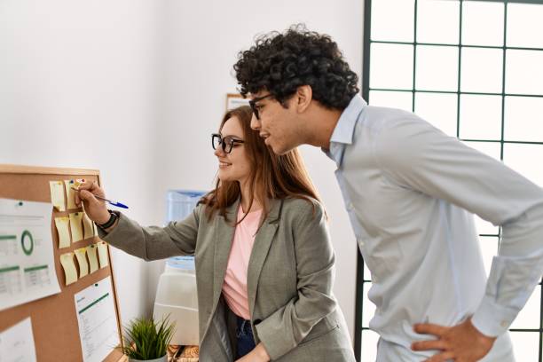 istock Two business workers smiling happy writing on corkboard reminder at the office. 1333968016