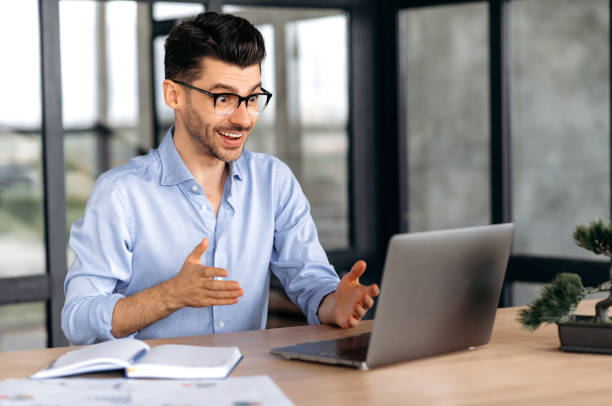 istock Video communication. Friendly handsome successful caucasian businessman, freelancer or manager, using laptop, talks to colleagues or clients on a video conference, greeting with hand gesture, smile 1333969017