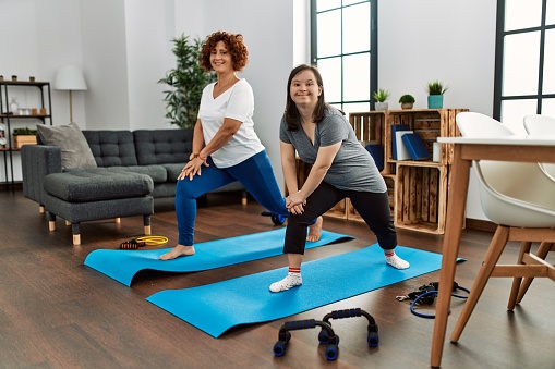 Mature mother and down syndrome daughter doing exercise at home. Stretching at the living room