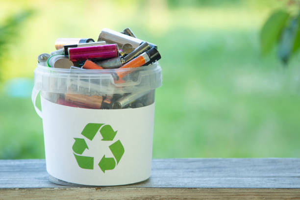 Battery recycle bin with old element on wood table on green grass background stock photo