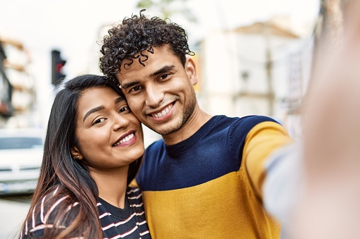 Young latin couple smiling happy and hugging make selfie by the camera at the city.