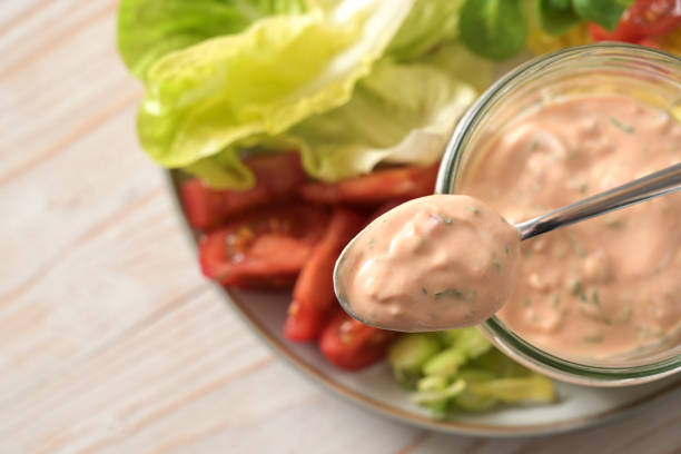 thousand island sauce based on skyr on a spoon and in a glass jar over slices of lettuce and tomato salad, healthy raw food meal, selected focus - salad food and drink food lettuce imagens e fotografias de stock