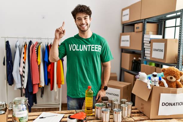 istock Hispanic man wearing volunteer t shirt at donations stand surprised with an idea or question pointing finger with happy face, number one 1333970708