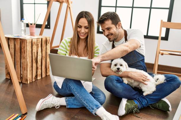 istock Two hispanic students smiling happy using laptop sitting on the floor with dog at art studio. 1333970809