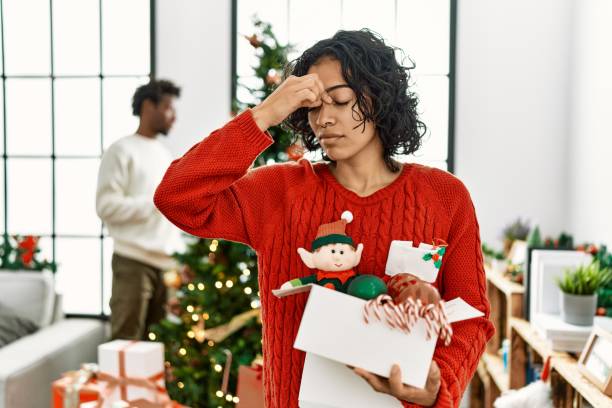 junge hispanische frau, die am weihnachtsbaum mit dekoration steht, müde reibende nase und augen, die müdigkeit und kopfschmerzen empfinden. stress- und frustrationskonzept. - stress stock-fotos und bilder