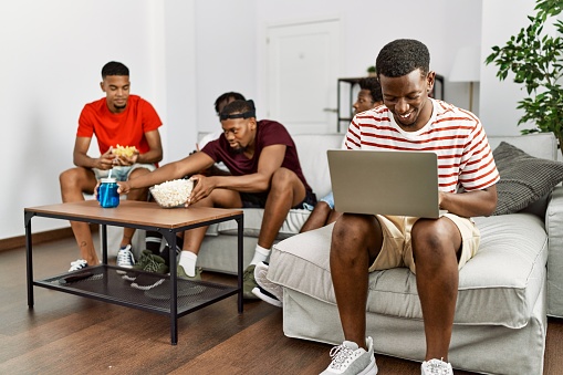 Group of african american people sitting on the sofa at home. Man smiling happy using laptop.