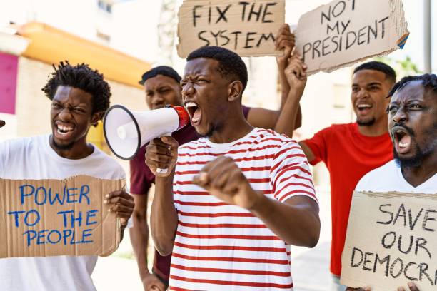 istock Group of young african american activists protesting holding banner and using megaphone at the city. 1333972545