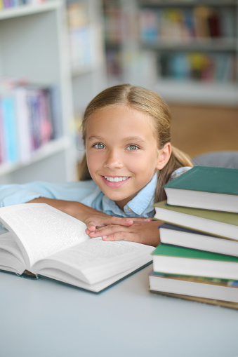 Portrait of a smiling contented young girl with an open book sitting at the desk