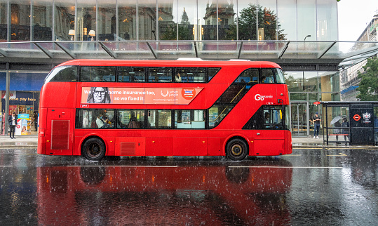 London, UK - A side view of a New Routemaster double decker bus on the street in London during heavy rainfall.