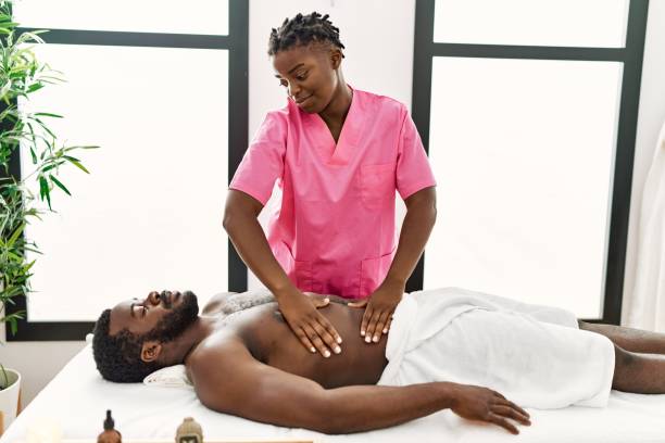 Young physiotherapist woman giving abdominal massage to african american man at the clinic. Young physiotherapist woman giving abdominal massage to african american man at the clinic. black male massage stock pictures, royalty-free photos & images