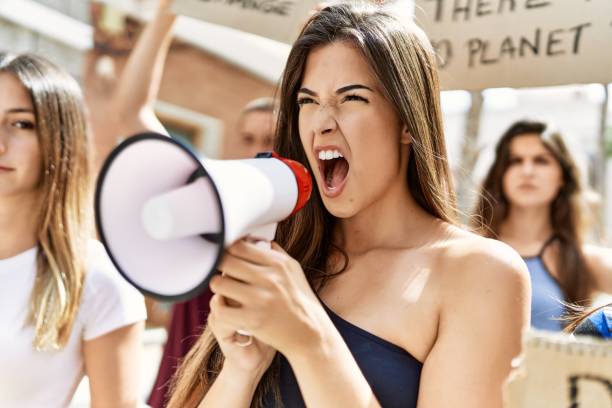 istock Group of young hispanic activists protesting holding banner and using megaphone at the city. 1333975671
